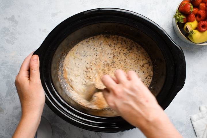 Steel cut oats being stirred with almond milk, bananas, chia seeds, flax seeds, and cinnamon.