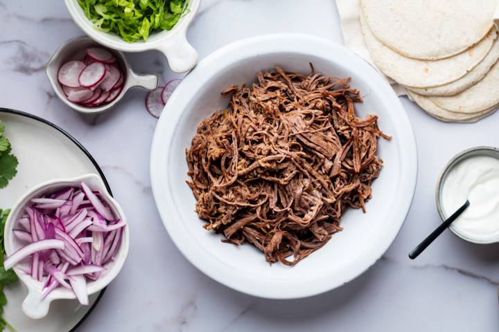 Shredded tri-tip in a bowl with taco ingredients on the side.