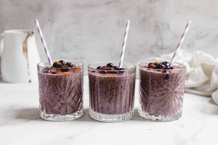 Fruit smoothie in three glasses with blueberries and straws.