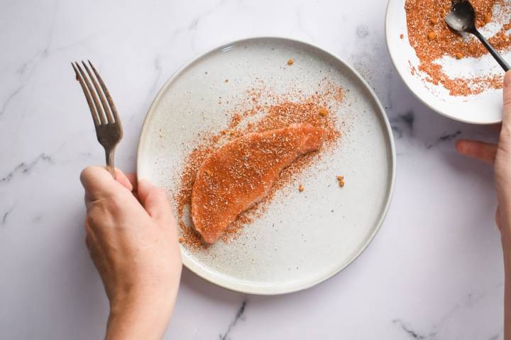 Center cut pork chips being coated with olive oil and a spice rub.