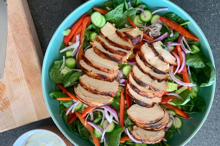 Spicy grilled chicken salad in a blue bowl with spinach and vegetables.