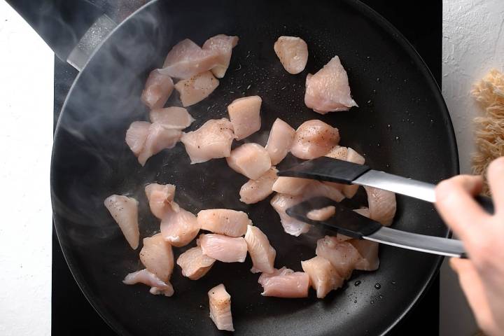 Chicken breast chunks cooking in a skillet with salt and pepper.