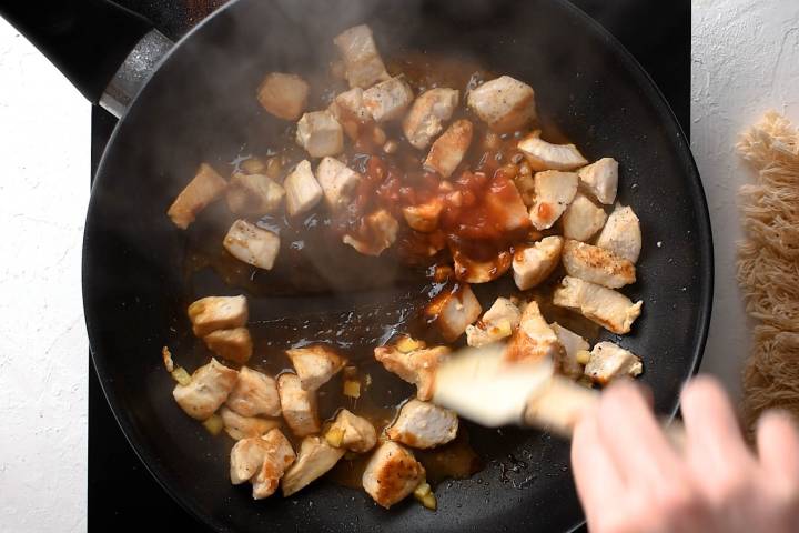 Hoisin sauce being stirred into a pan with chicken breast, garlic, and ginger.