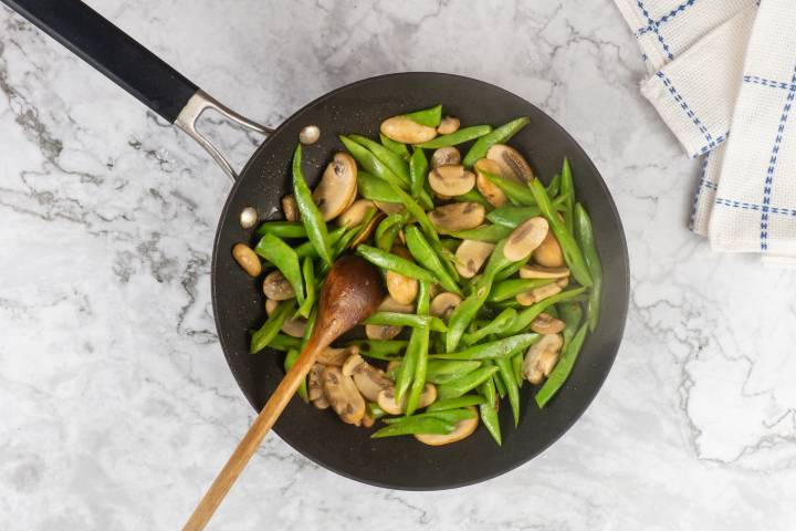Green beans and mushrooms cooking in a skillet with a wooden spoon.