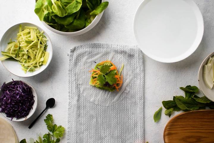 Lettuce, carrots, red cabbage, mint, cilantro, and basil being layered on a spring roll wrapper.
