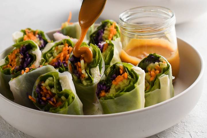 Fresh spring rolls being drizzled with peanut sauce.