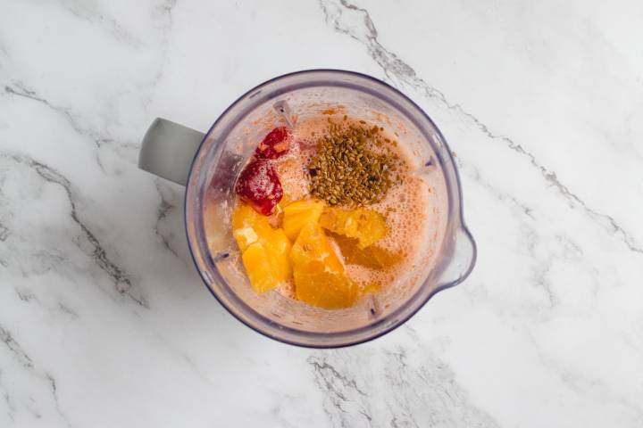 Strawberries, mango chunks, flaxseeds, carrots, and almond milk in a blender.
