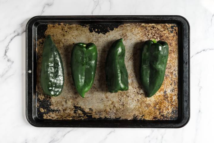 Poblano peppers on a baking sheet that will be roasted in the oven.