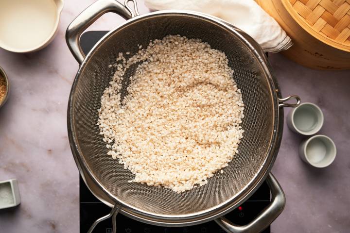 Sushi rice being rinsed in a strainer.