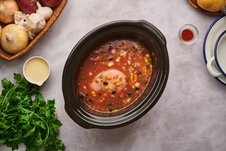 Chicken breast, beans, tomatoes, corn, and onions in a slow cooker for taco soup.