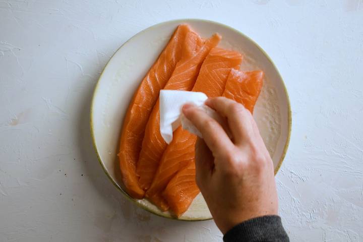 Salmon filets being patted dry with a paper towel.