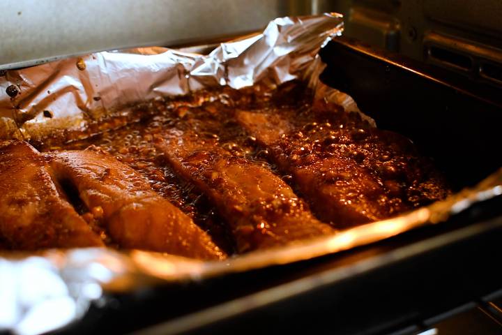Teriyaki salmon being broiled in the oven on a baking dish with foil.