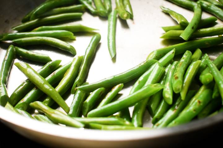 Green beans being cooked in coconut oil in a pan.