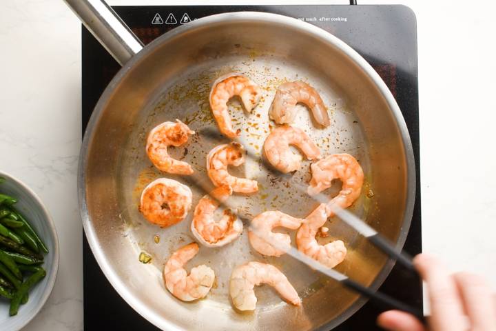 Shrimp being cooked in a skillet with coconut oil.