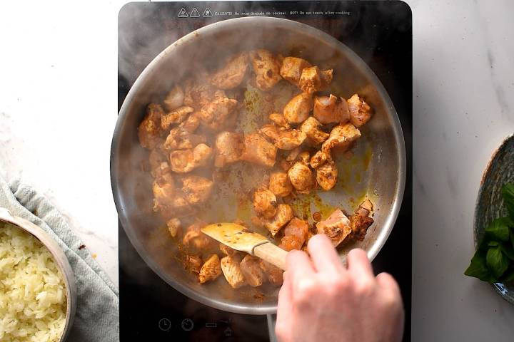 Chicken cooking in red curry paste in a skillet.