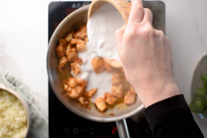 Coconut milk being added to a skillet or Thai red curry chicken.