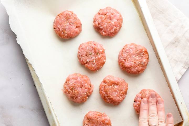Raw turkey sausage patties on a baking sheet with parchment paper.