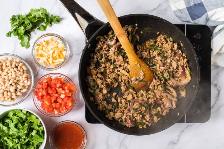 Ground turkey and poblano peppers cooking in a skillet with spices and tomato paste.
