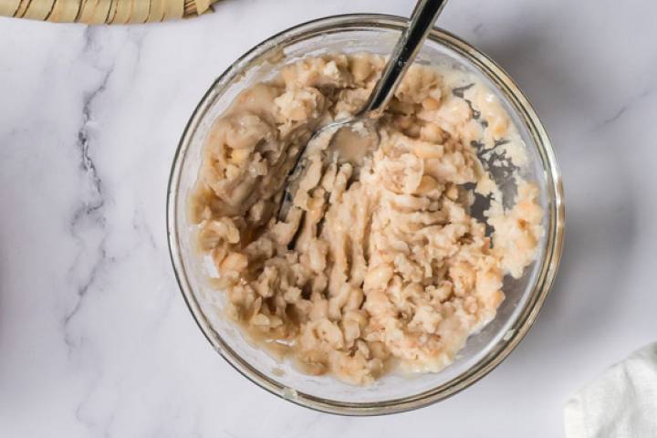 Pinto beans being mashed with a fork in a bowl.