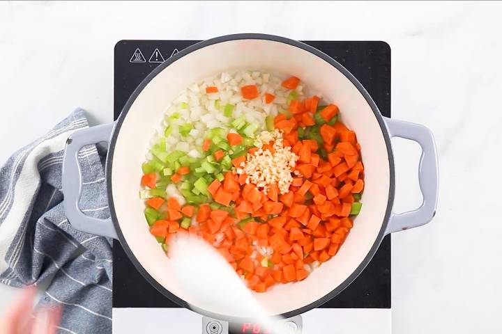 Stirring onion, celery, carrots, and garlic on a soup pot over an electric burner.