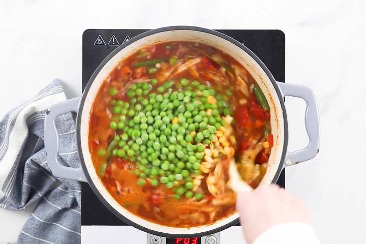 Stirring in the corn and peas to make this vegetable soup.