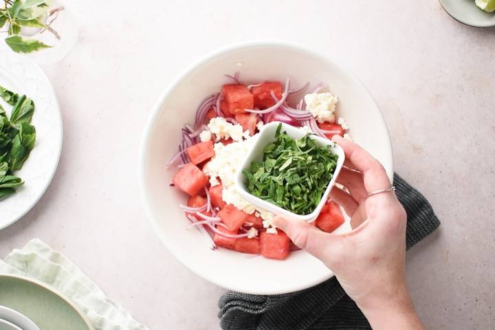 Fresh mint being added to a bowl of watermelon and feta cheese.