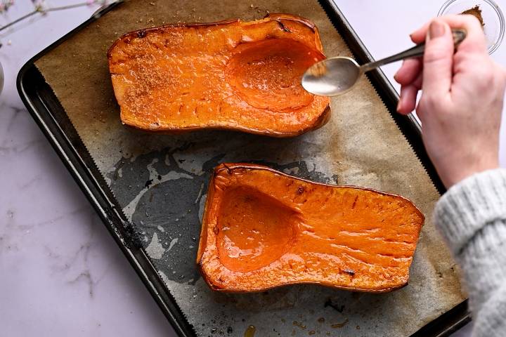 Whole roasted butternut squash being drizzled with butter and brown sugar to make a glaze.