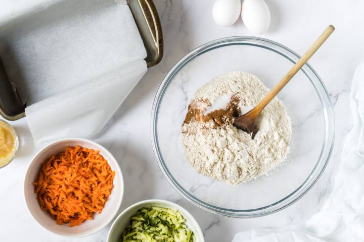 Whole wheat flour, salt, baking soda, cinnamon, and nutmeg being stirred in a bowl.