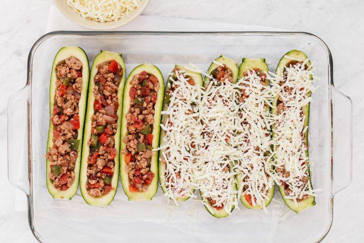 Zucchini stiffed with taco meat and sprinkled with shredded cheese in a baking dish.