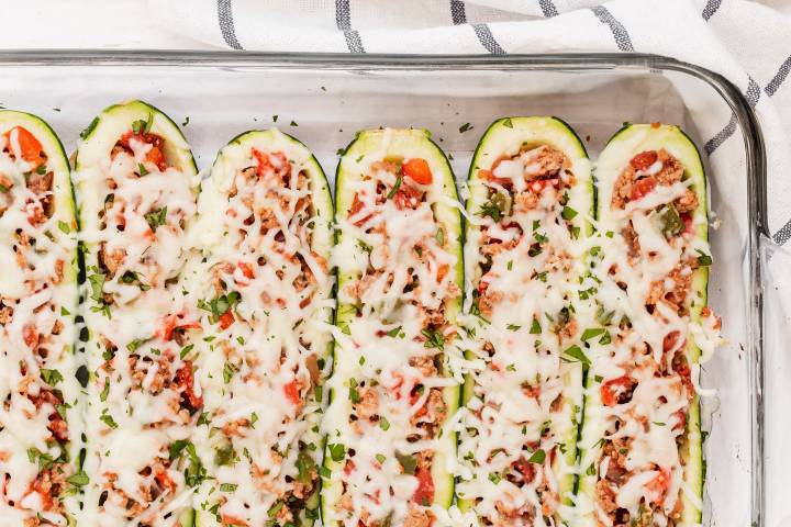 Baked zucchini taco boats with melted cheese in a glass baking sheet.