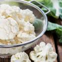 A bowl of cauliflower florets and a cutting board.
