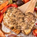 Roasted chicken thigh on a wooden spatula with vegetables.