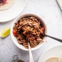 Mexican shredded beef in a bowl with tomatoes and chipotle peppers with tacos on the side.