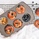 Almond flour yogurt blueberry muffins in a muffin tray with extra blueberries and walnuts on the side.