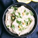 Artichoke hummus with lemon and chickpeas in a bowl with a blue napkin.