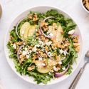 Arugula salad with sliced pears, toasted walnuts, red onions, goat cheese, and vinaigrette tossed in a ceramic bowl.