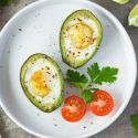 Two avocado baked eggs on a cutting board with salt and pepper.