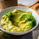 Avocado hummus in a bowl with cilantro and sliced fresh avocado.