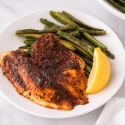 Baked blackened tilapia in a baking dish with lemon slices and blackening seasoning.