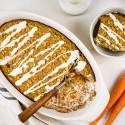 Baked carrot cake oatmeal with a cream cheese glaze in a baking dish with shredded coconut and oats.