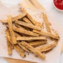 Baked eggplant fries with a crispy Parmesan and breadcrumb coating on a plate with ketchup.