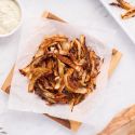 Baked onion straws with a crispy Parmesan coating on parchment paper with dipping sauce on the side. 