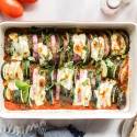 Baked ratatouille with sliced eggplant, zucchini, red onions, and tomatoes in a baking dish with melted cheese and fresh basil.
