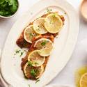 Baked red snapper with spice rub and lemon slices on a plate with sweet potatoes, lemon wedges, and parsley on the side.