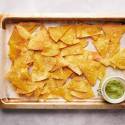 Baked tortilla that are golden browned served on a baking sheet with homemade guacamole.