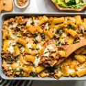 Baked ziti with ground beef, tomatoes, zucchini, and melted cheese in a baking dish.