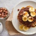 Banana oat pancakes made with mashed bananas and rolled oats stacked on a plate with maple syrup. 