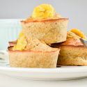 Banana muffins with quinoa and chia seeds with a sliced banana on top stacked on a plate.
