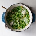 Sauteed peas with garlic, shallots, lemon, and shredded Parmesan cheese in a ceramic dish.