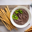 Black bean hummus in a bowl with cilantro with breadsticks and pretzels on the side.